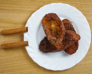 Geleneksel ev yapımı İspanyol Torrijaları iki tarçın çubuğuyla süslenmiş beyaz bir tabakta. Üst Görünüm