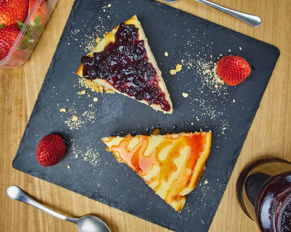 Set of cheesecakes with a Strawberry, Strawberry sauce drip, crumbled cookies and two strawberries on a black slate board. Top View