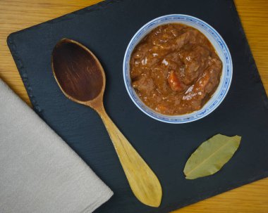 Fricando, geleneksel Katalan tapa, ahşap kaşık, peçete ve siyah tahta tahtada defne yaprağı ile süslenmiş bir kasede sığır güveci. Üst görünüm