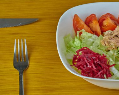 Ton balığı ve yeşil vejetaryen salatası ahşap bir arka planda gümüş reveransla süslenmiş.