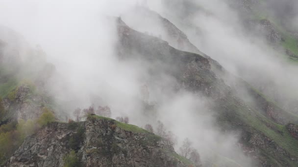 ロシア。春先に霧と雲の中央コーカサス山脈の険しい山の斜面に忍び寄るの密なベールがピークします。. — ストック動画