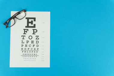 Gözlükler ve mavi arka planda bir görüş testi masası.