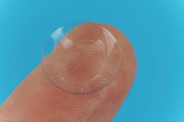 Mavi arka planda kontak lensli bir parmak. Yakın plan.