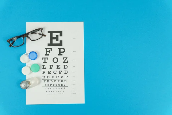 Gafas, lentes y una mesa de pruebas de visión a la izquierda sobre un fondo azul —  Fotos de Stock