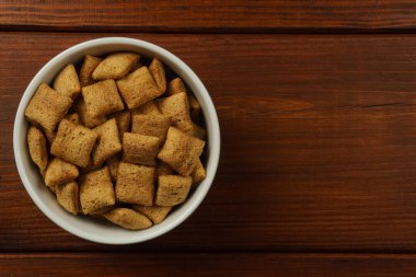 Koyu bir masada beyaz bir kasede çikolatalı kahvaltı pedleri. Üst görünüm