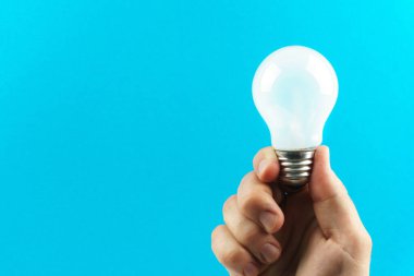 Bir adam mavi arka planda beyaz bir ampul tutuyor.