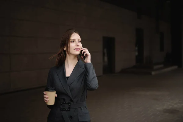 Young businesswoman with coffee talking on the phone on the street
