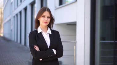 İş elbisesi giymiş güzel bir kadın kollarını göğsünde kavuşturuyor..