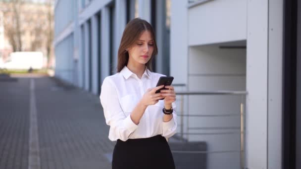 Joven hermosa chica sonriente responde a un mensaje en su teléfono móvil — Vídeos de Stock