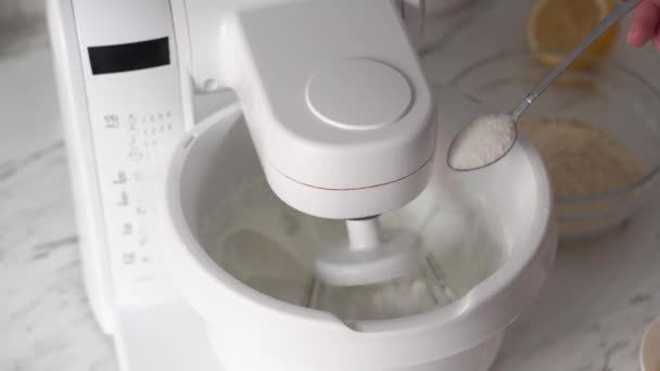 Add sugar with a spoon to a working mixer.Sugar being pouring into bowl.Close-up — Stock Video