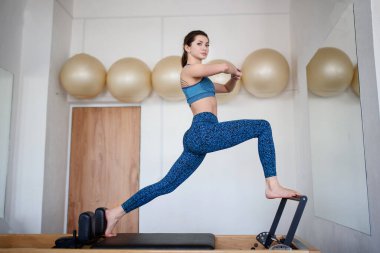 Genç bir atletik kadın jimnastik salonunda bir reformcu üzerinde egzersiz yapıyor..