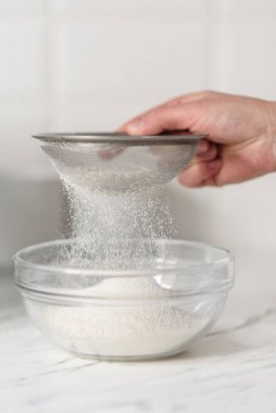 Bir kadının elleri, süzgeçten un geçirirken yakın plan çekimleri..