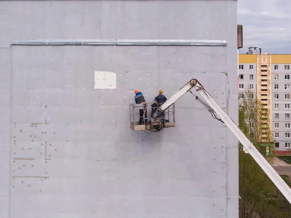 Двое рабочих стоят на воздушной платформе и изолируют стену дома — стоковое фото
