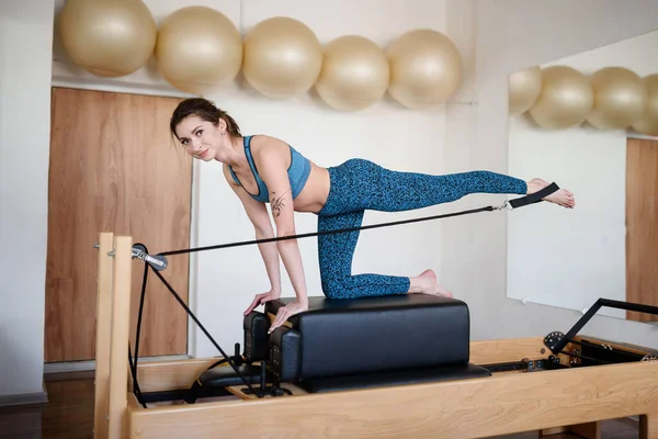 Mladá žena ve sportovním oblečení dělá Pilates na reformátora, zvedá nohu — Stock fotografie