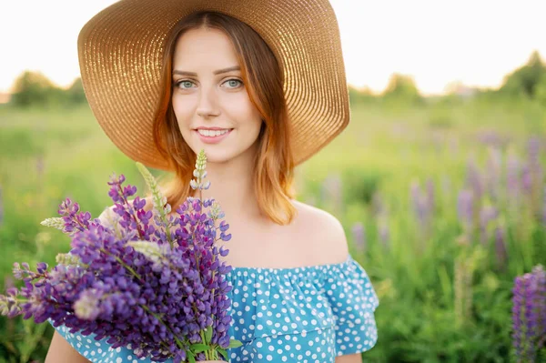 Una hermosa mujer caucásica en un sombrero sostiene un ramo de altramuces y sonrisas. — Foto de Stock