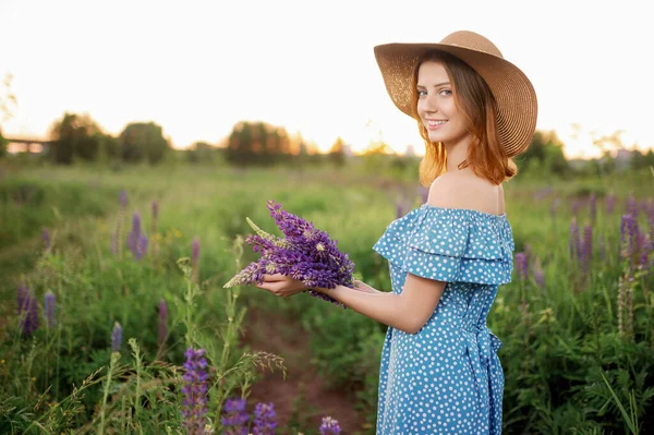 Una hermosa mujer caucásica con sombrero y vestido sostiene un ramo y sonríe. — Foto de Stock