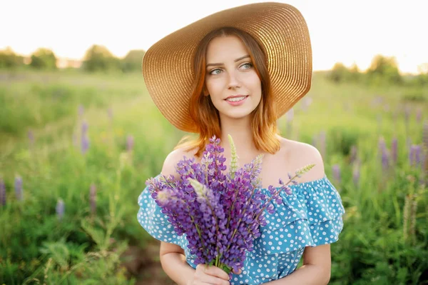 Una hermosa mujer caucásica en un sombrero sostiene un ramo de altramuces y sonrisas. — Foto de Stock