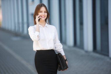 İş merkezinin yakınında cep telefonuyla konuşan mutlu güzel bir kadın.