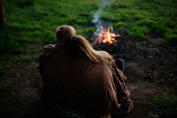 Birbirine aşık bir çift battaniyeyle oturmuş ateşe bakıyor. Stok Fotoğraf