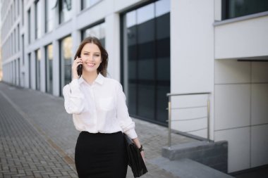 İş merkezinin yakınında cep telefonuyla konuşan mutlu güzel bir kadın.
