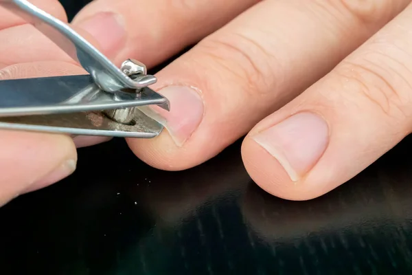 hand manicure with nail clipper. close up over black background. self-cutting nails. close-up nail cutting