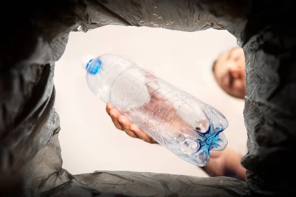 Plastic bottle waste, for recycling. Concept of the problem of plastic waste disposal. A man throws an old used bottle into a black trash can