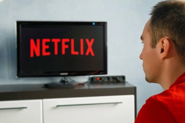 Genç bir adam evinde ve televizyonunda Netflix izliyor. Önplanda TV kumandası, TV 'de bulanık arkaplan.
