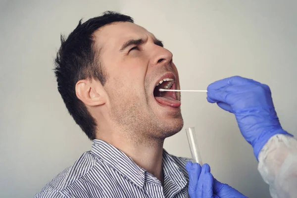 Doctor Doing Coronavirus Test For male Patient. DNA test. Collection of mucus from the throat for research in the laboratory. Taking a saliva sample from a man. PCR polymerase chain reaction