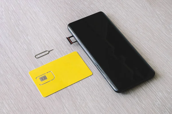 Cartela SIM și tava de card microSD cu instrument de eliminare la partea laterală a smartphone-ului pe masa de lemn. spațiu liber pentru design și text — Fotografie, imagine de stoc