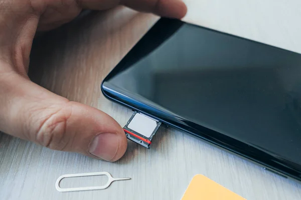 Plateau carte SIM et carte microSD avec outil de retrait sur le côté du smartphone sur une table en bois. espace libre pour le design et le texte — Photo