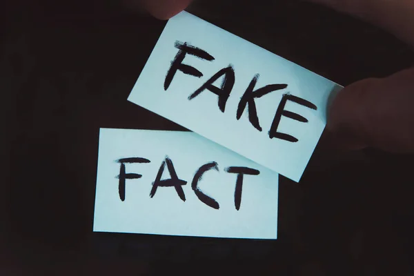 Substitution of concepts. The fact is replaced by a fake. a man changes the signs with the words fact on fake on a black background. — Stock Photo, Image