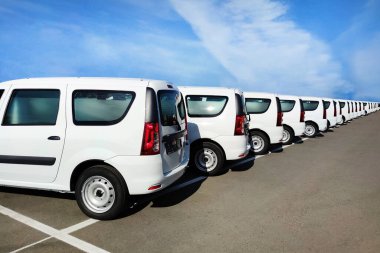 Otoparkta satılık beyaz minibüsler. Otoparkta sıra sıra bekleyen arabalar.