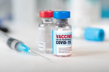 İki şişe Cavid 19 Coronavirus aşısı ve beyaz masada bir şırınga. Covid-19 salgınıyla mücadelenin tıbbi konsepti.