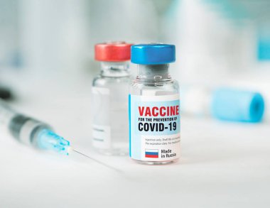 İki şişe Cavid 19 Coronavirus aşısı ve beyaz masada bir şırınga. Covid-19 salgınıyla mücadelenin tıbbi konsepti.