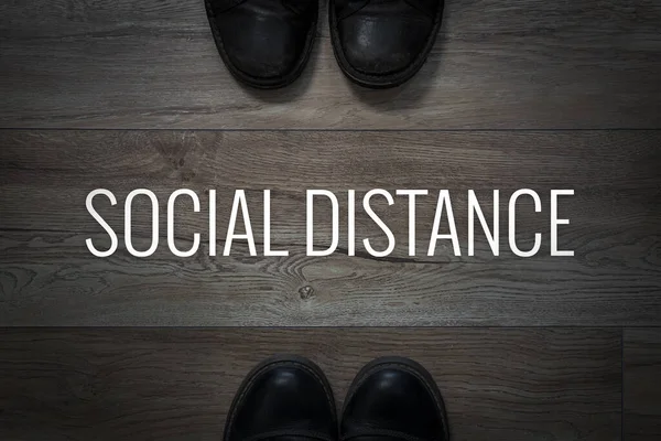 The concept of social distancing. Shoes on the floor and the inscription social distance on the background of the floor on a dark background. Dangerous distance. Violations of personal space