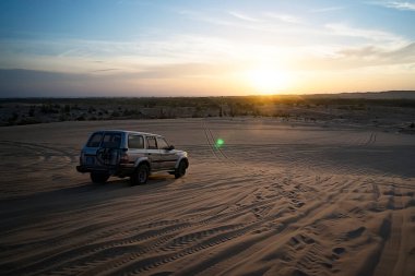 Çöl 'de renkli bir gün batımı. Çöldeki kum tepelerinde yükselen güneş ışınlarında off-road arabaları sürüyor..