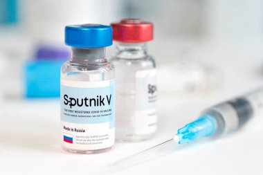 Koronovirüs enfeksiyonundan elde edilen Sputnik V aşısı mavi arka planda ve masada bir şırınga. 18 Ocak 2021, Barnaul, Rusya.