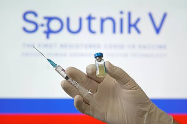 Koronovirüs enfeksiyonundan elde edilen Sputnik V aşısı covid-19 ve arka plandaki Rus bayrağında doktorun elinde bulunan şırınga. 18 Ocak 2021, Barnaul, Rusya.