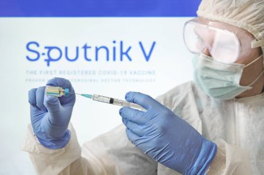 Bir doktor, Sputnik V logosunun arka planında Coronavirus covid 19 'a karşı aşı hazırlıyor. 18 Ocak 2021, Barnaul, Rusya.