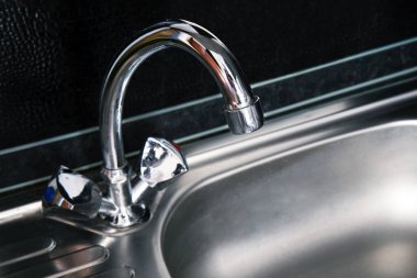 Metalden yapılmış sıcak kaynak suyu için gri, temiz lavabo ve musluk. Modern mutfak lavabosu koyu siyah arka planda.