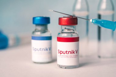 Koronovirüs enfeksiyonundan elde edilen Sputnik V aşısı mavi arka planda ve masada bir şırınga. 18 Ocak 2021, Barnaul, Rusya.