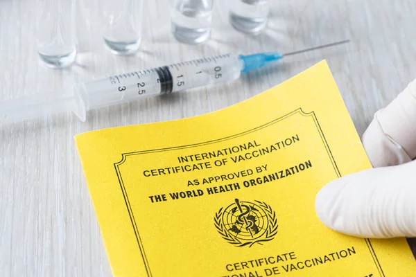 international certificate of vaccination a document for recording the vaccines made. the document is a yellow color. passport of a foreign citizen and a syringe on the table. concept of safe travel.
