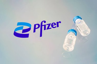 A vaccination syringe and a glass ampoule with a clear liquid on a blue background with the logo of pfizer pharmaceutical company. March 15, 2021. Barnaul, Russia. clipart