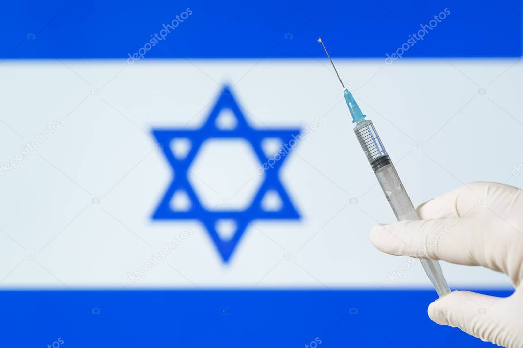 the doctor's hand holds a syringe against the background of the Israeli flag. The concept of mass vaccination against covid 19 coronavirus in the country.
