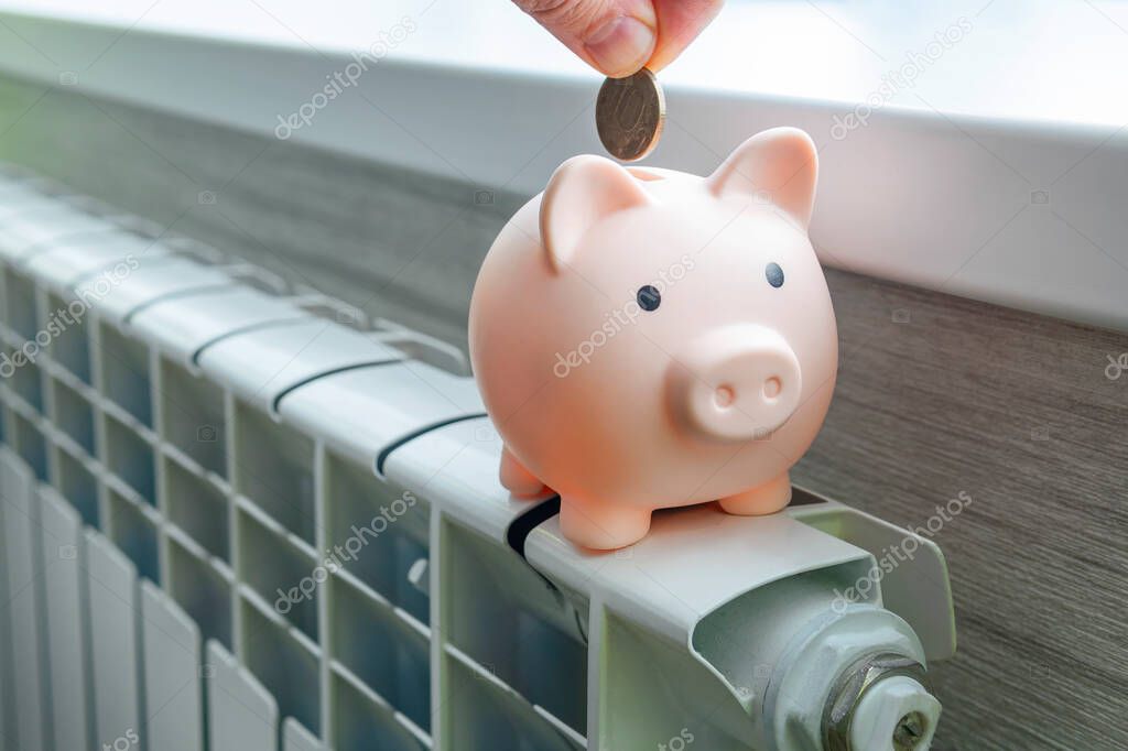 The concept of paying for heating in homes with a cold climate. piggy bank pig on a white metal radiator. The concept of saving on utilities