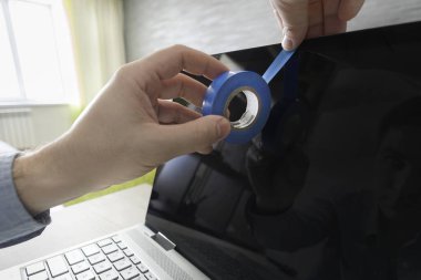 İnsan eli yapışkan bir bantla bilgisayar kamerasını engelliyor. Eziyet manyaklığı, işkence kompleksi, zulüm yanılsaması. Web kamerasıyla mahremiyeti gözetlemek.