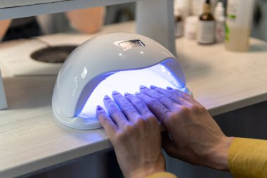 UV lambası jöle cilası manikür süreci. Salon prosedürü. Bir kadın evde tırnaklarını kurutuyor..