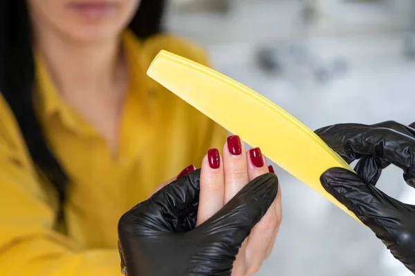 Beauty industry concept. Woman manicurist master in gloves is polishing client's nails using file. Portrait of working young female in cosmetology salon, clinic. Hygiene and care for hands.