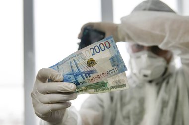 Koruyucu maskeli bir doktor ve hastanedeki virüs geçirmez giysi para sayıyor. Kırmızı bölgedeki çalışanlara yapılan ödemeler. Düşük maaşla tehlikeli bir iş. Covid hastalarla çalışan doktorlara ödül