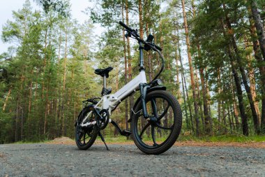 Çevre dostu ulaşım aracı. Elektrikli motoru olan bir bisiklet. Yeşil bir ormanın arka planında beyaz renkli elektrikli bir bisiklet..